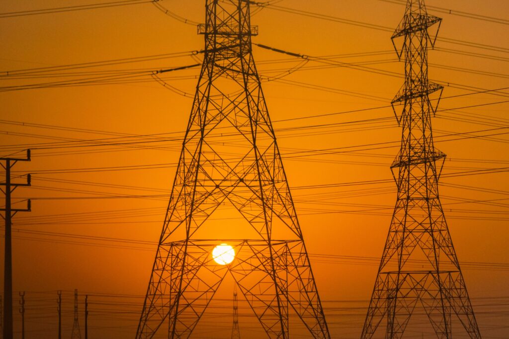 Silhouetted electric towers set against a deep orange sunset sky, capturing serene industrial beauty.
